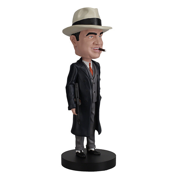 3/4 right side view of Al Capone bobblehead, wearing a white fedora, dark trench coat, and suit, holds a gun with a smirk. The base is labeled "Al Capone." Retro and playful tone.