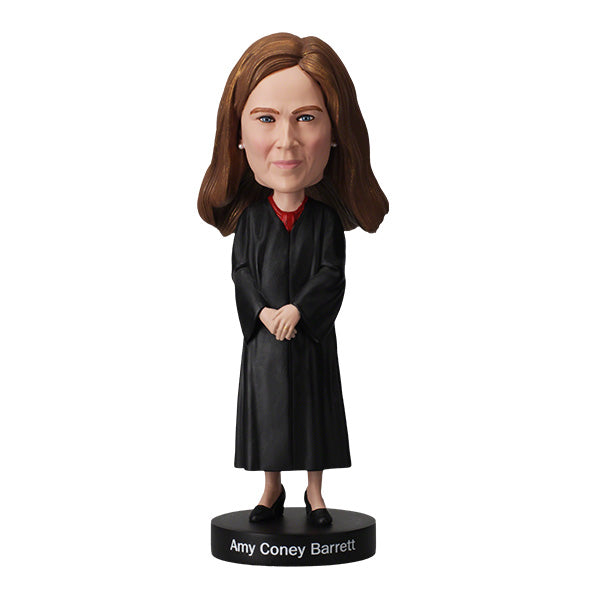 Amy Coney Barrett Bobblehead figure is wearing judicial robes and long brown hair, standing on a base labeled "Amy Coney Barrett," conveying authority.