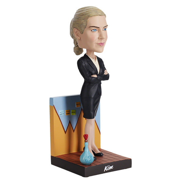 3/4 Right side view of Better Call Saul Kim Wexler Bobblehead features a woman in a black suit with arms crossed, standing confidently in front of a chart backdrop. A blue bottle with a red cap is at her feet.