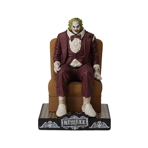 A figurine of a character dressed in a maroon suit with green hair sits on a patterned chair. The base says "Beetlejuice," suggesting a playful tone.
