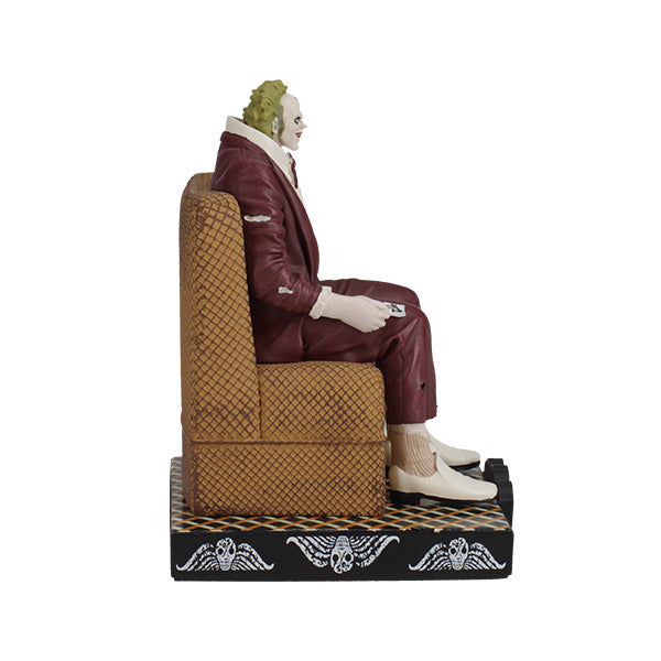 Right side view figurine of a character dressed in a maroon suit with green hair sits on a patterned chair. The base says "Beetlejuice," suggesting a playful tone.