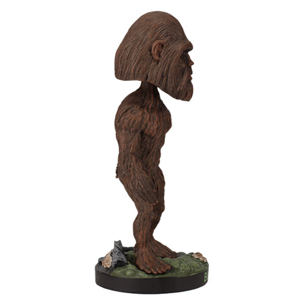 Side view of Bigfoot Bobblehead figure of Bigfoot with brown fur, large head, and detailed features standing on a green, rocky base labeled "BIGFOOT" in green letters.