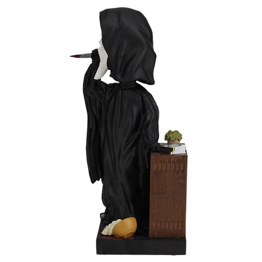 Statue of a figure in black robes with a book and plant on a white background