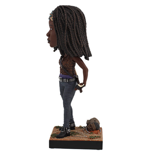 Left view Michonne bobblehead in headband and vest holding sword on labeled base.