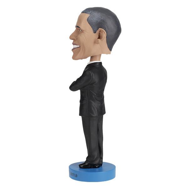 Left side view of Barack Obama bobblehead figurine dressed in a black suit and red tie, standing on a blue base labeled "Barack Obama".