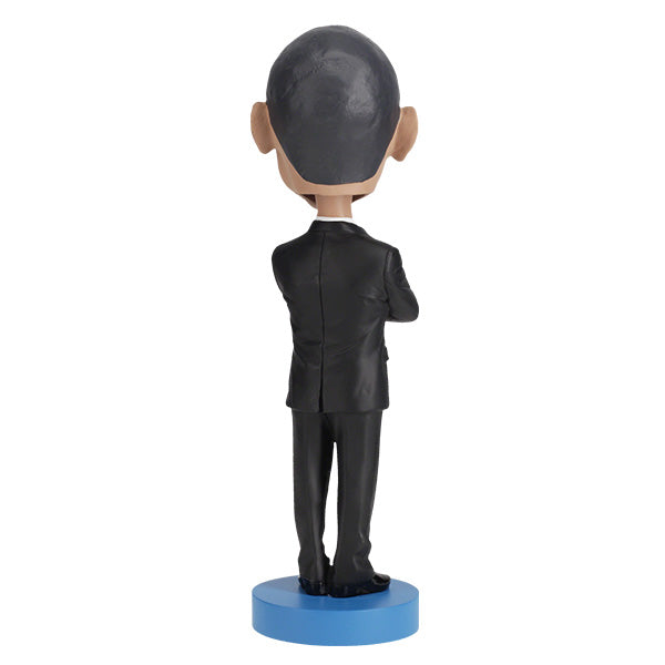 Back view of Barack Obama bobblehead figurine dressed in a black suit and red tie, standing on a blue base labeled "Barack Obama".