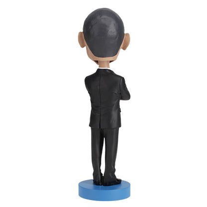 Back view of Barack Obama bobblehead figurine dressed in a black suit and red tie, standing on a blue base labeled "Barack Obama".