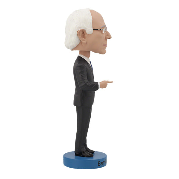 Right side view of Bernie Sanders Bobblehead figurine of an elderly man with white hair and glasses, wearing a dark suit, standing on a base labeled "Bernie Sanders." The figure has a calm expression.