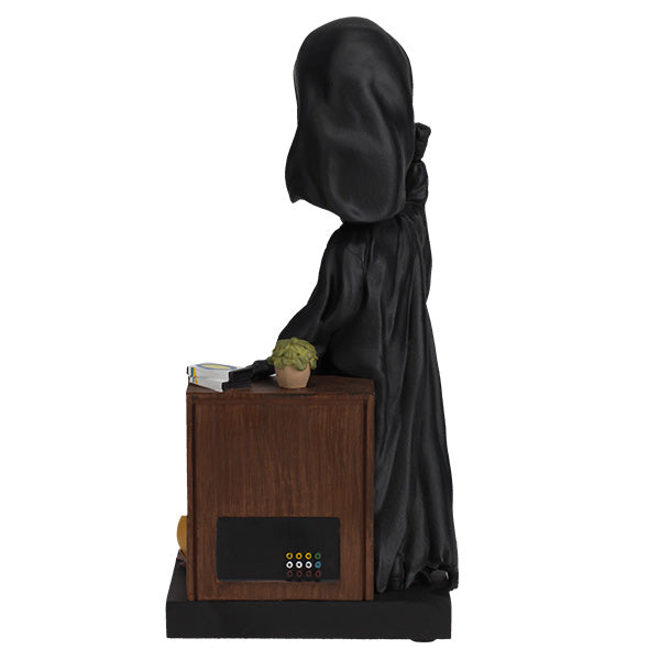Statue of a hooded figure standing next to a wooden table with a plant on a white background