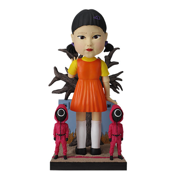 Young-hee in orange and yellow dress with two small pink-hooded figures and leafless tree.